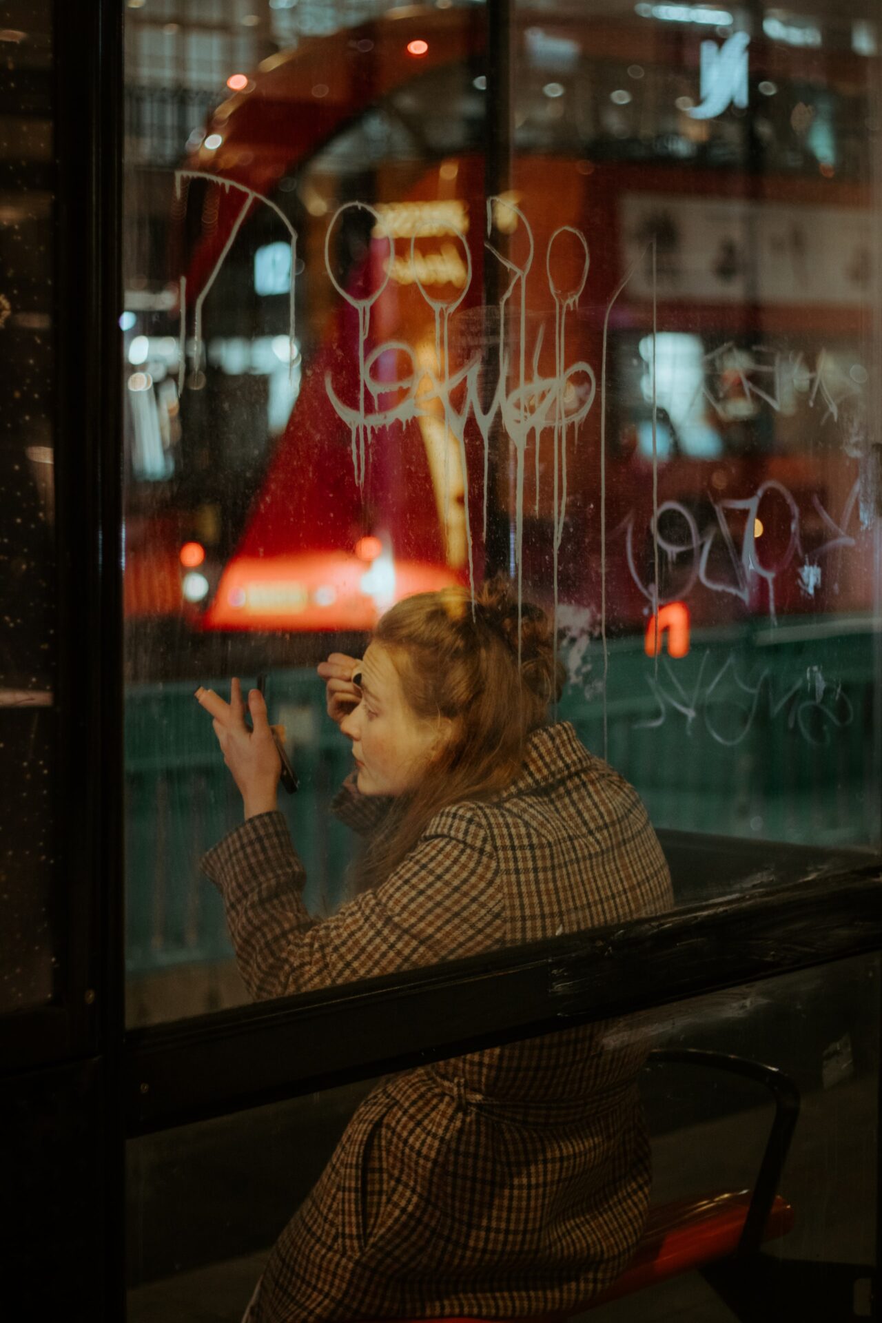 redhead girl in bus stop doing make up and a glass with graffiti