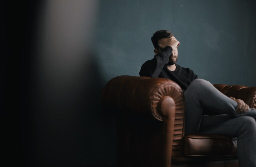 a man sitting on a couch with a hand on his face, sad