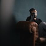 a man sitting on a couch with a hand on his face, sad